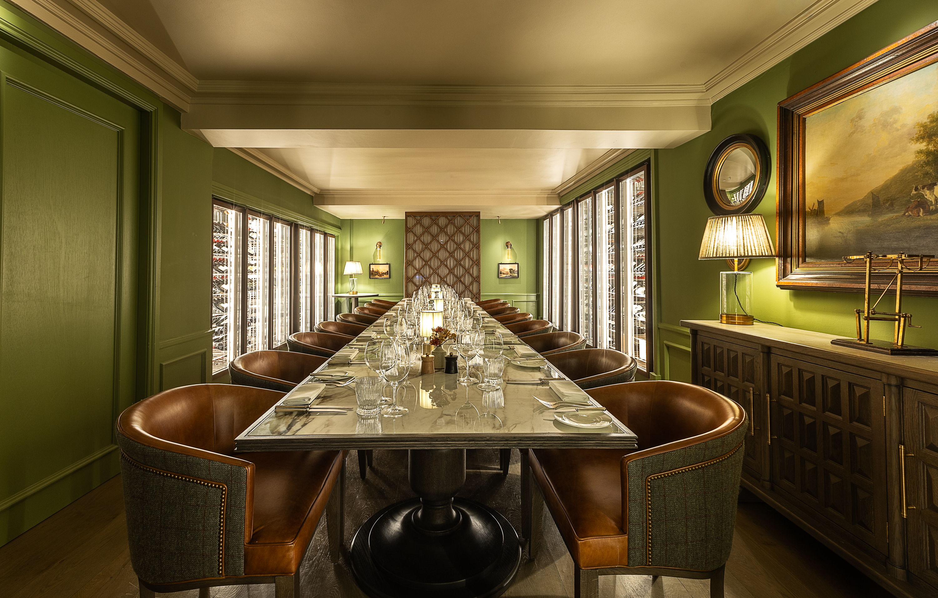 Elegant private dining room with a long marble table, leather chairs, warm lighting, and wine displays lining the walls