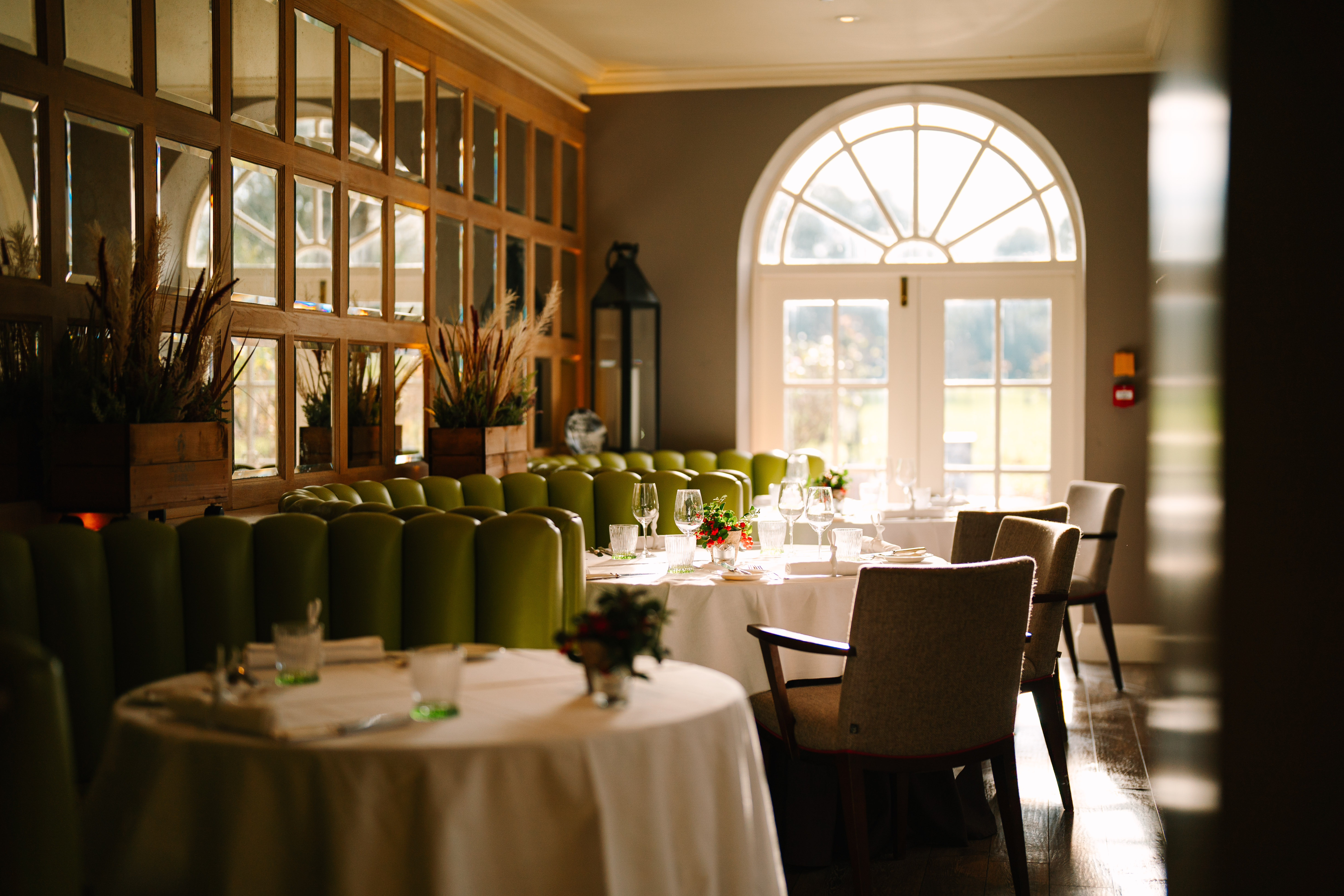 Stylish restaurant with green chairs and arched window.